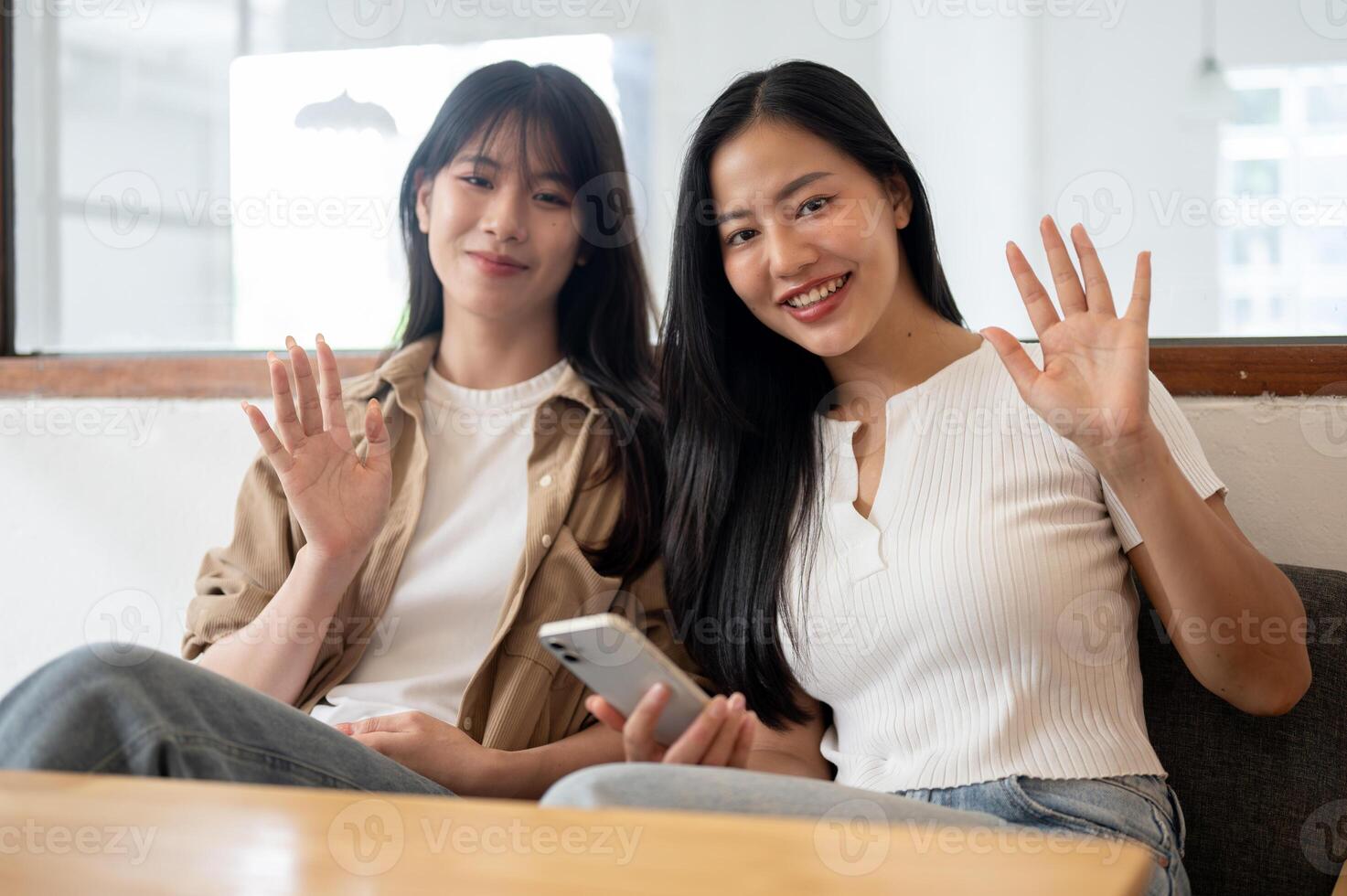 A portrait of two beautiful Asian women sitting on a sofa in a coffee shop, smiling at the camera. photo