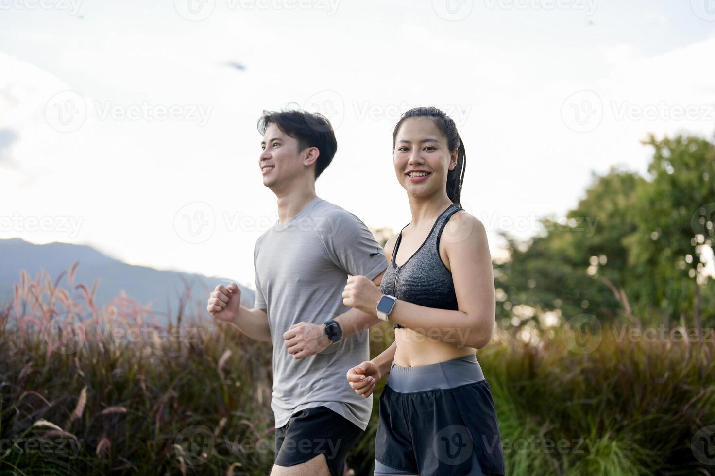Sporty Asian girl in sportswear is smiling at the camera while running with her boyfriend in a park. photo