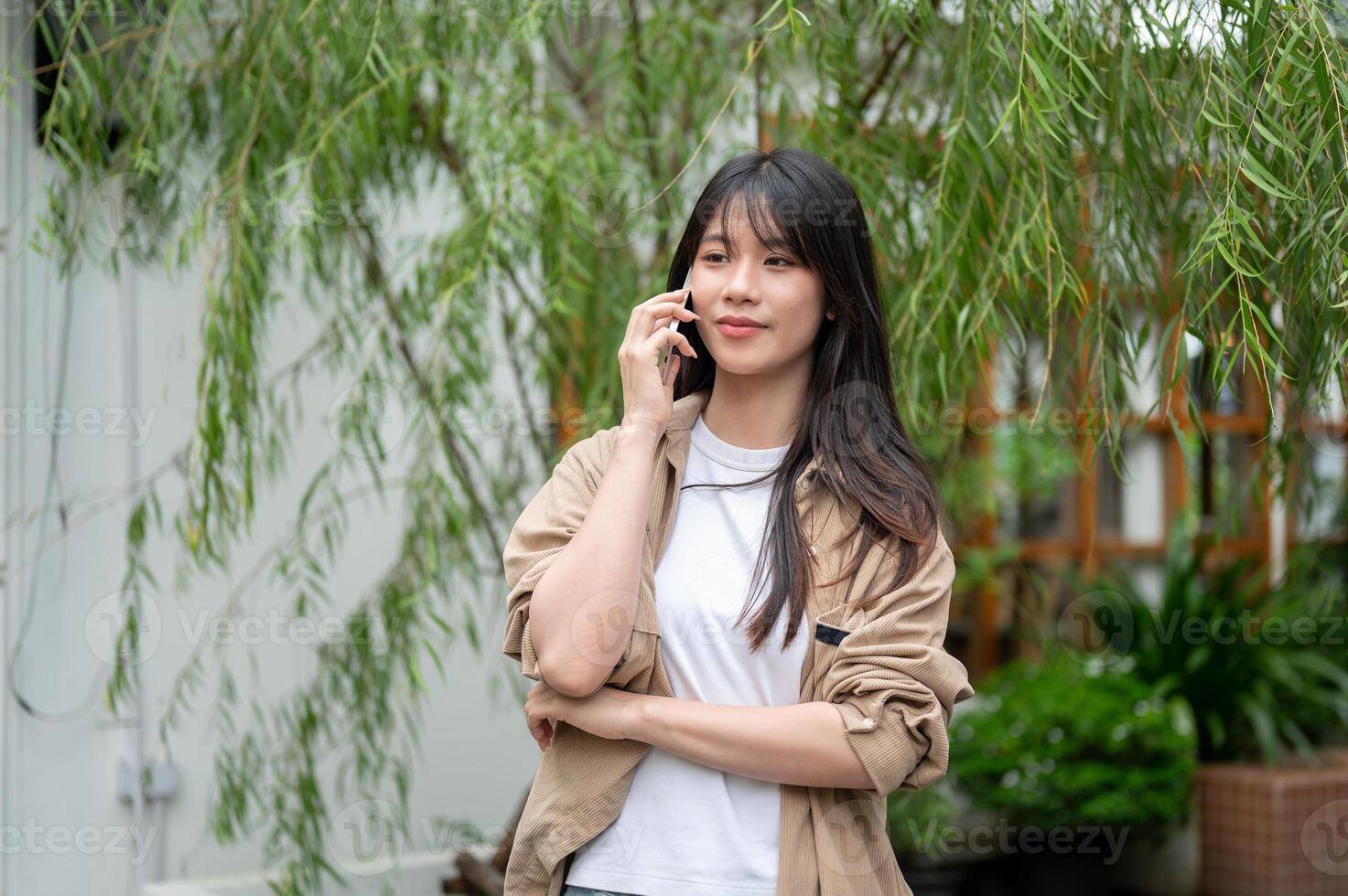 A charming young Asian woman is talking on the phone while walking through her home garden. photo