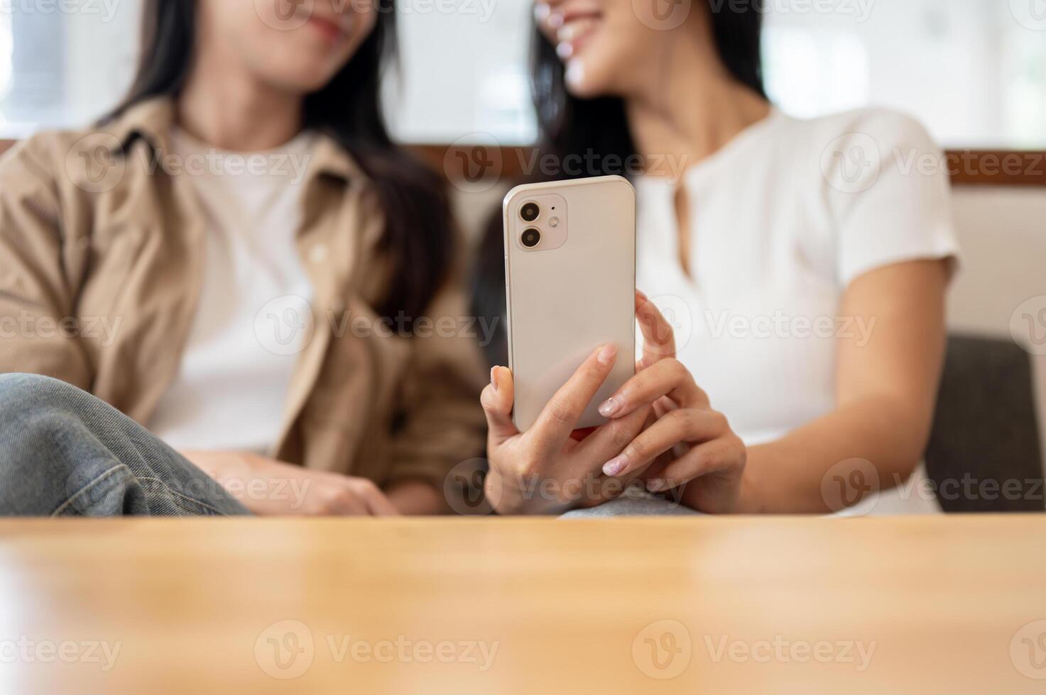 Two happy female friends enjoying a conversation while watching something on a smartphone together. photo