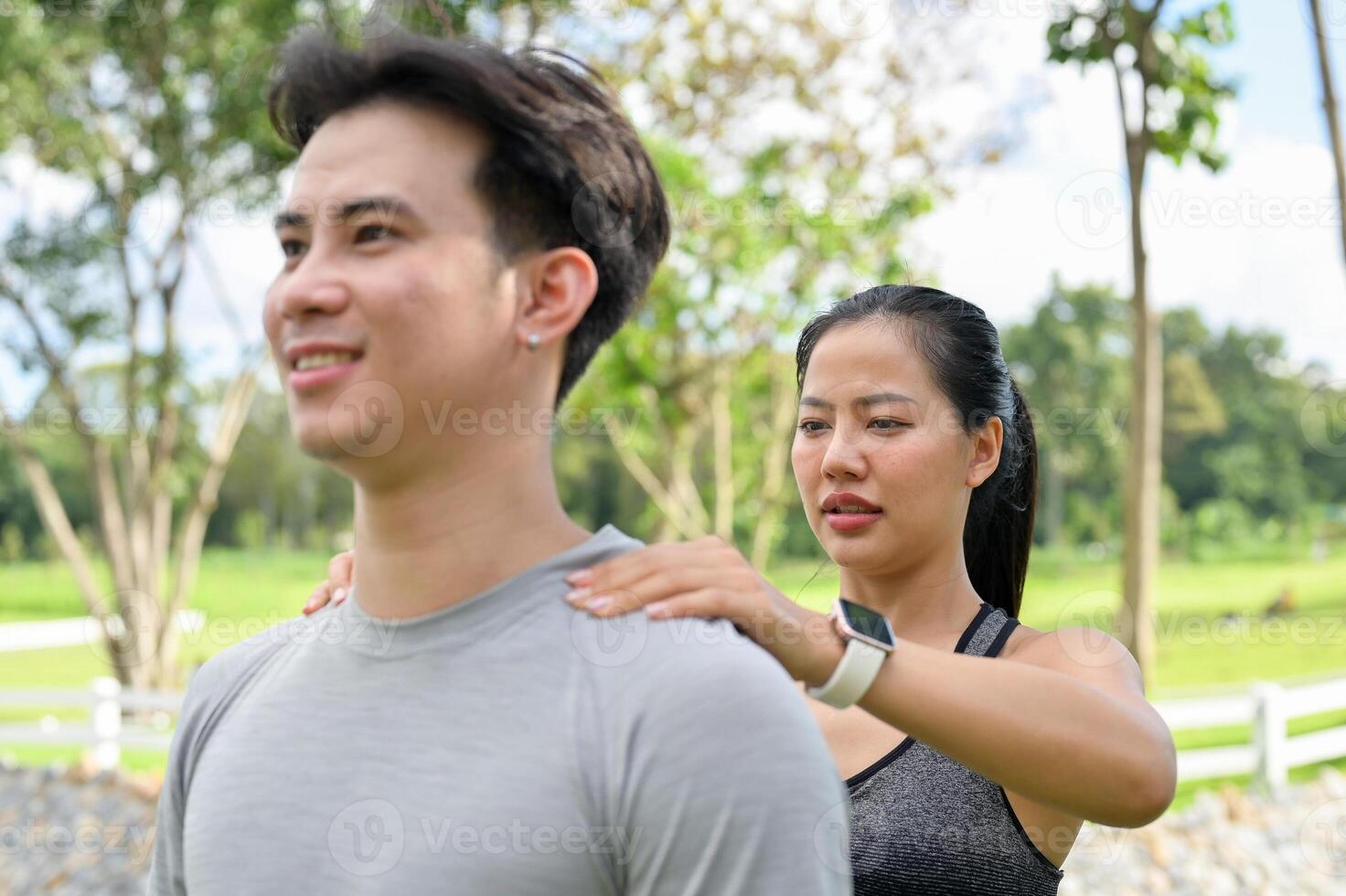 A woman is massaging her boyfriend's shoulders after jogging together in a public park. photo