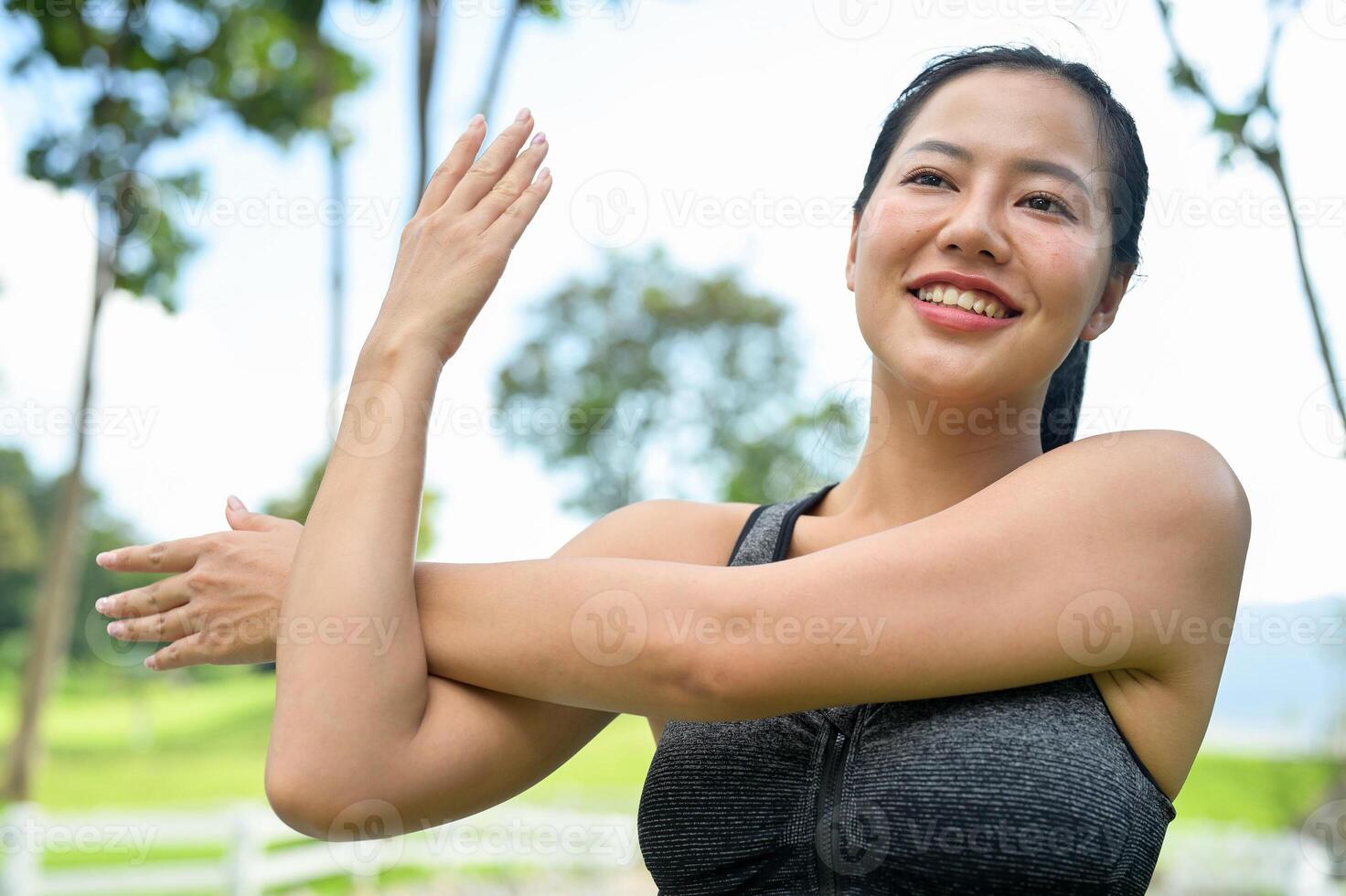 A fit, and healthy Asian woman in sportswear stretches her arm, warming up before jogging in a park. photo