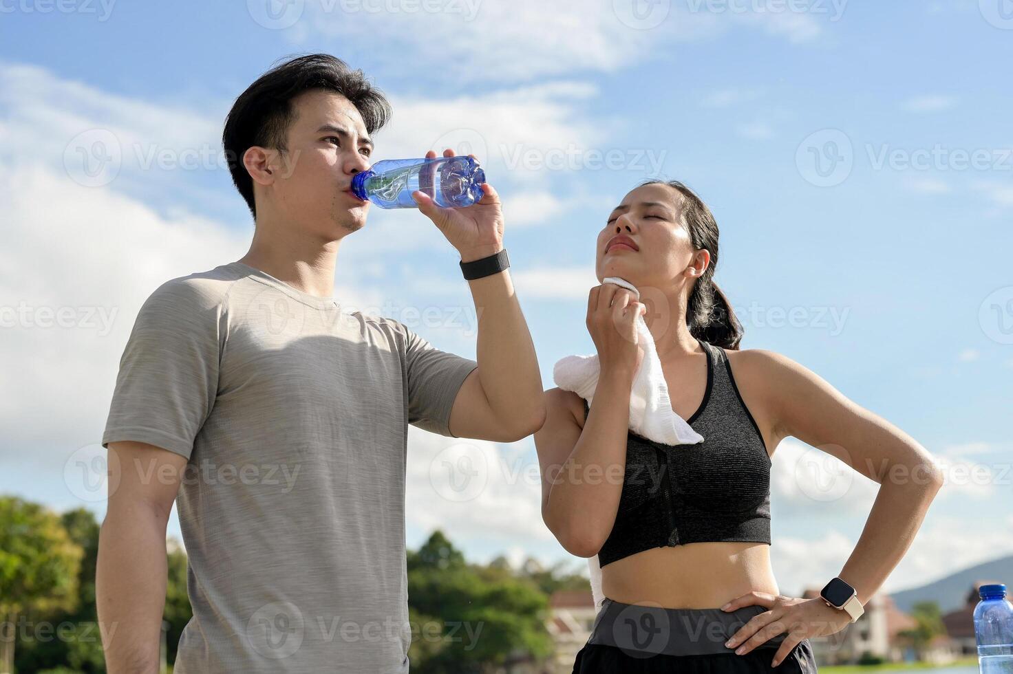 A tired, sweaty couple in sportswear is resting together after a long run in a park on a sunny day. photo