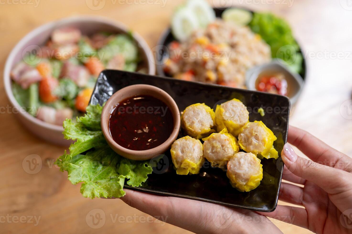 A close-up of a woman's hand holding a plate of pork dumpling dim sum above a table in a restaurant. photo