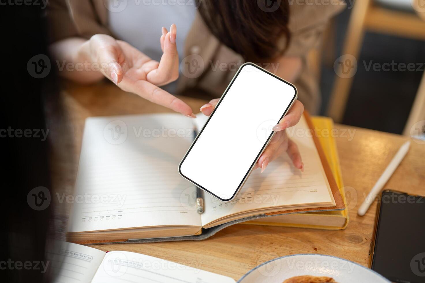 A close-up of a woman showing her smartphone to a friend while discussing work, at a table indoors. photo