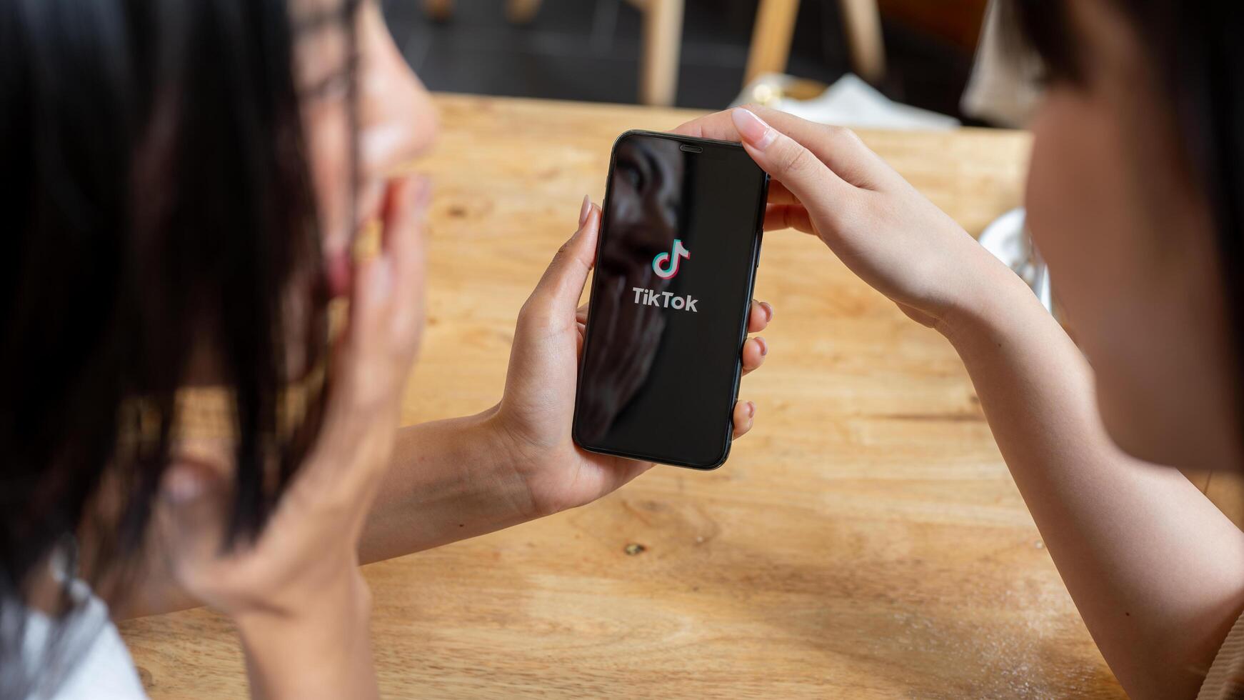 Two cheerful Asian women are enjoying talking while watching a content on the TikTok app. photo