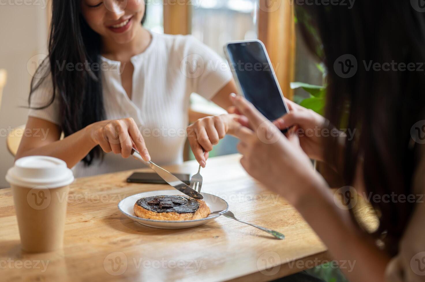 A close-up of a girl taking a picture of a dessert with her smartphone while her friend is eating. photo