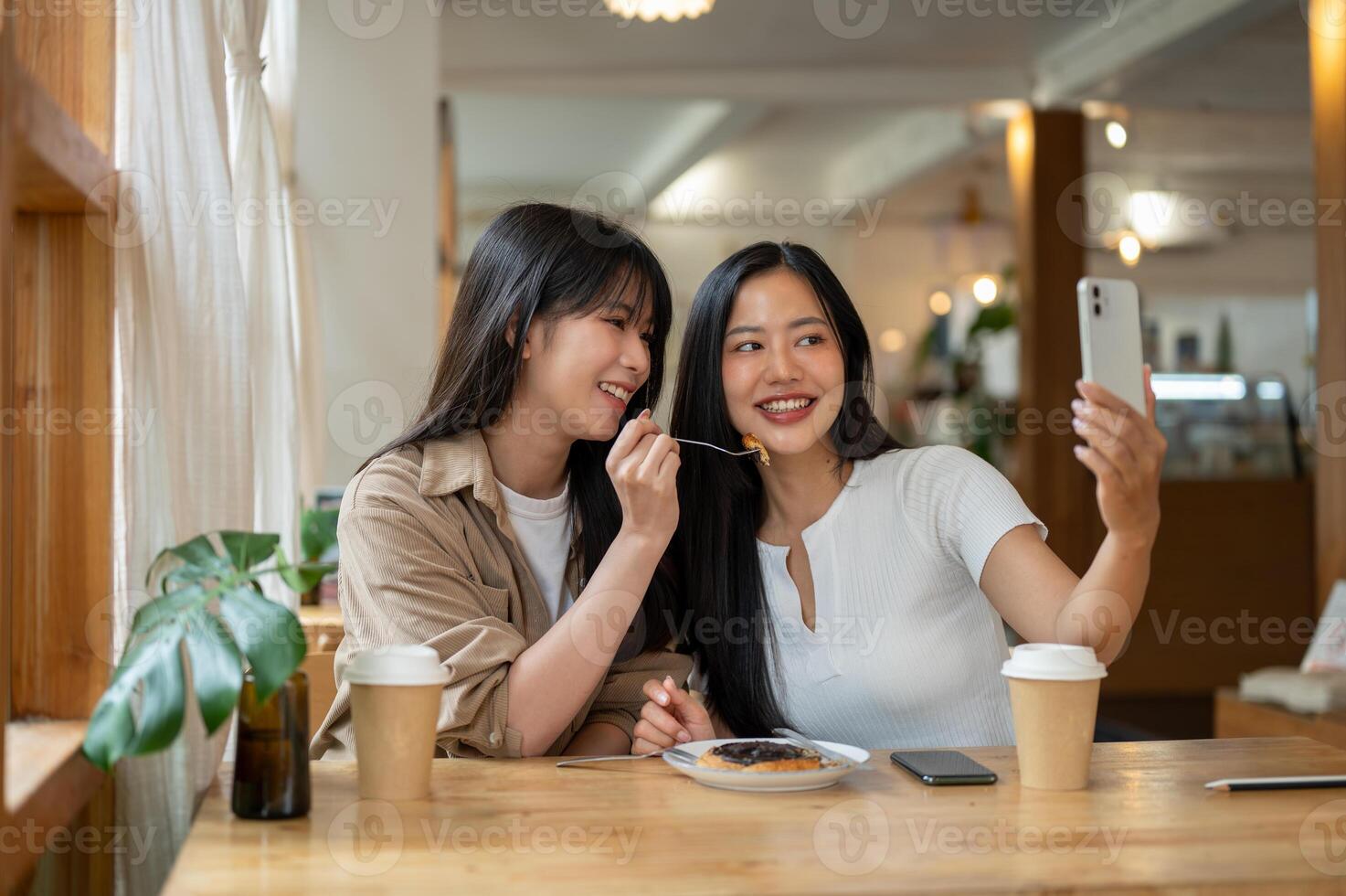 Two beautiful Asian women are enjoying taking pictures together while hanging out at a coffee shop. photo