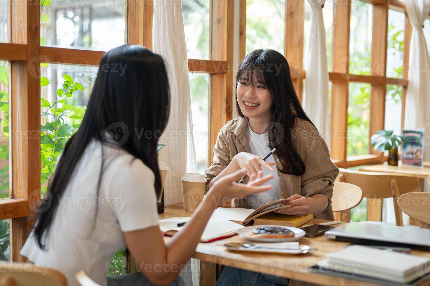 Two cheerful Asian college students are enjoying talking and reading together in a coffee shop. photo