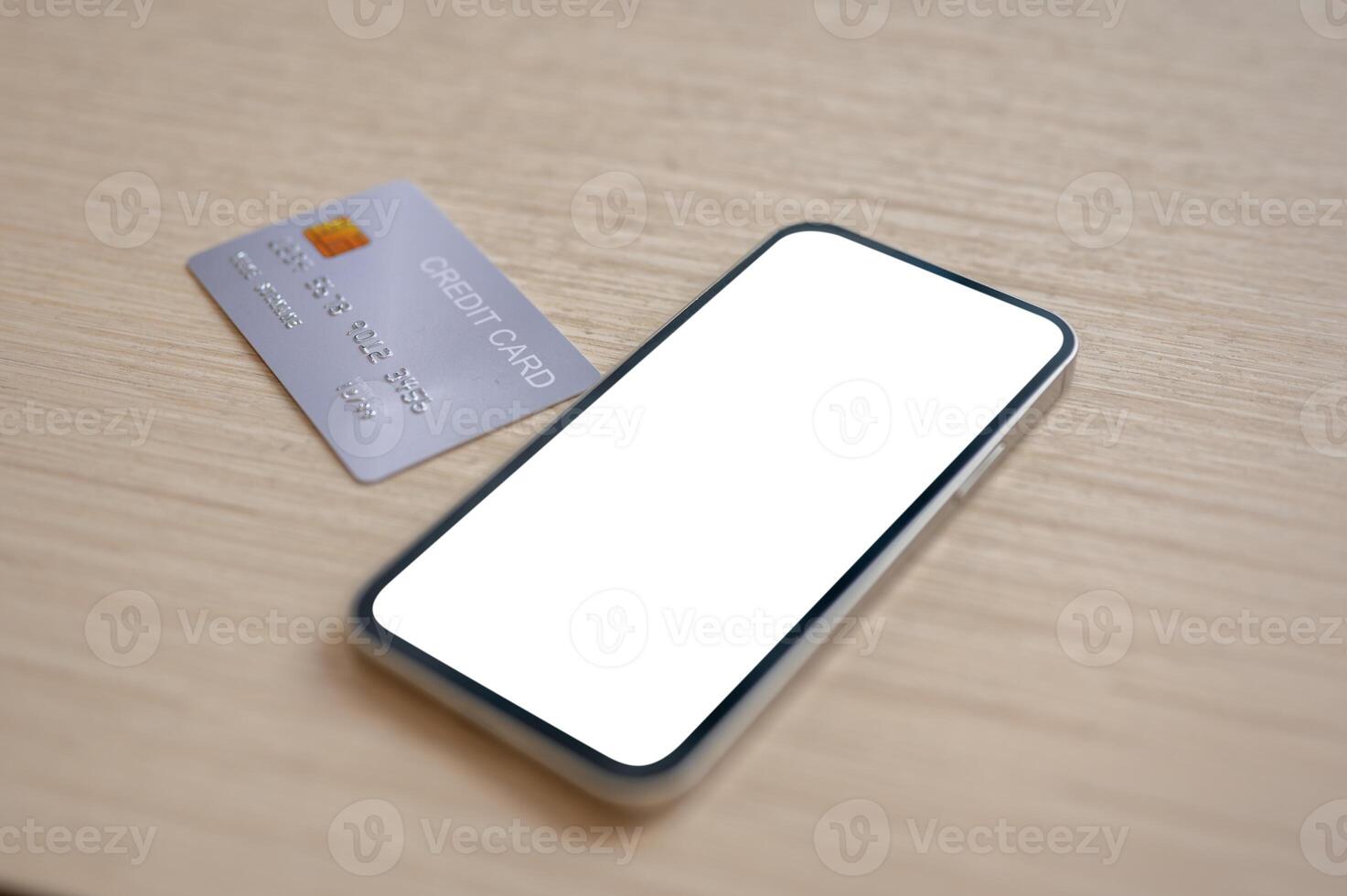 A close-up of a credit card and a smartphone with a white screen mockup placed on a wooden table indoors. photo