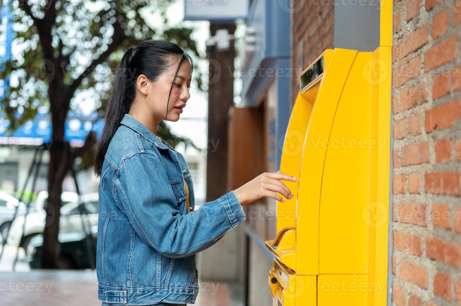 A side view of a beautiful Asian woman inserting her debit card into an ATM to withdraw some money. photo