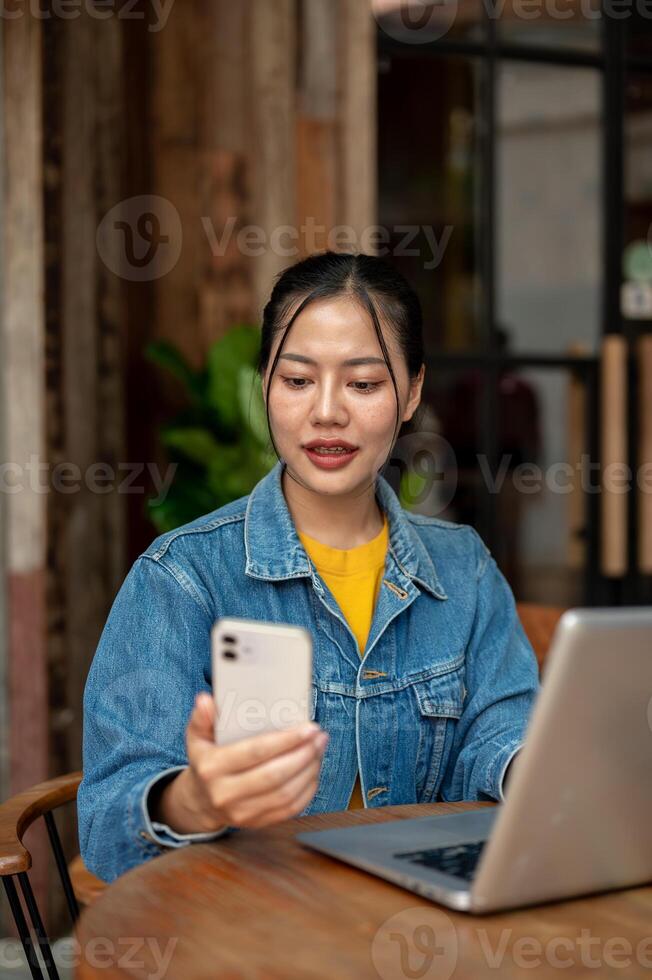 A beautiful Asian woman is checking text messages on her smartphone while sitting in a coffee shop. photo