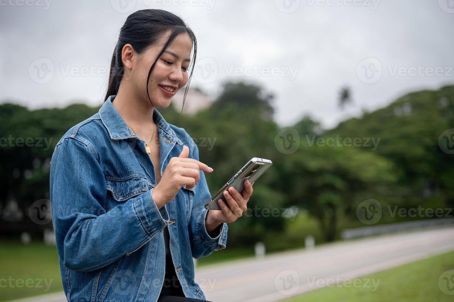 A beautiful Asian woman is using her smartphone while relaxing on a bench in a park. photo