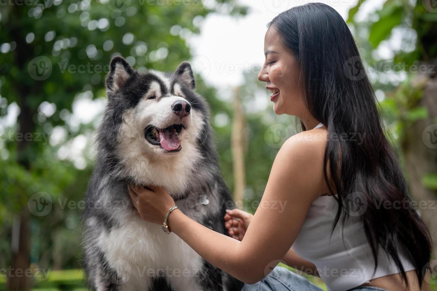 A happy Asian woman is talking and playing with her dog, enjoying a fun moment together in a park. photo