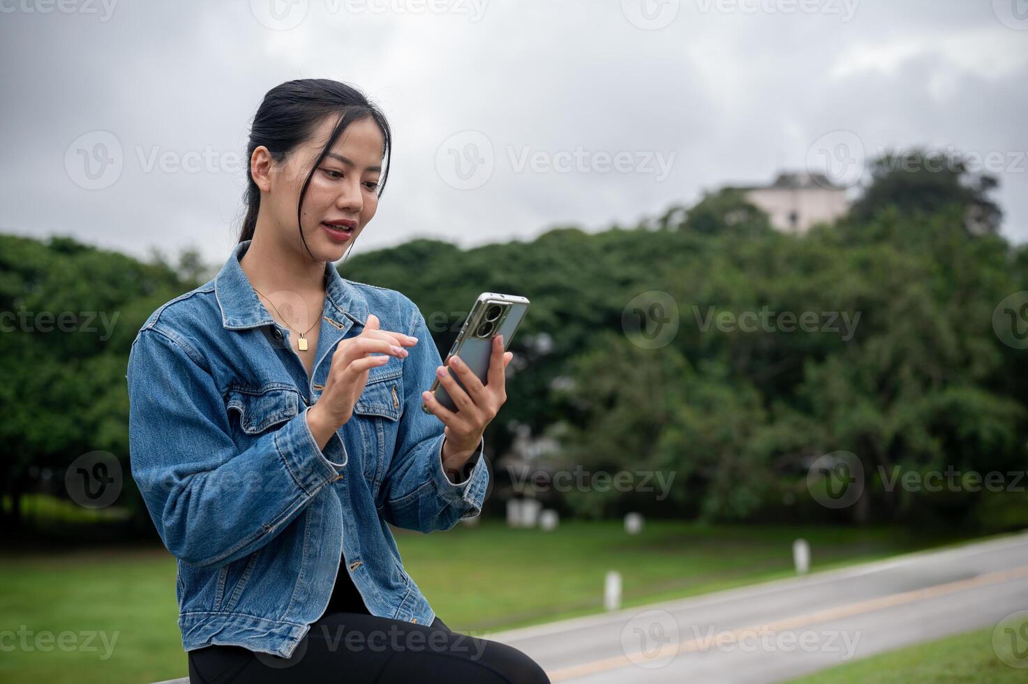 A beautiful Asian woman is using her smartphone while relaxing on a bench in a park. photo