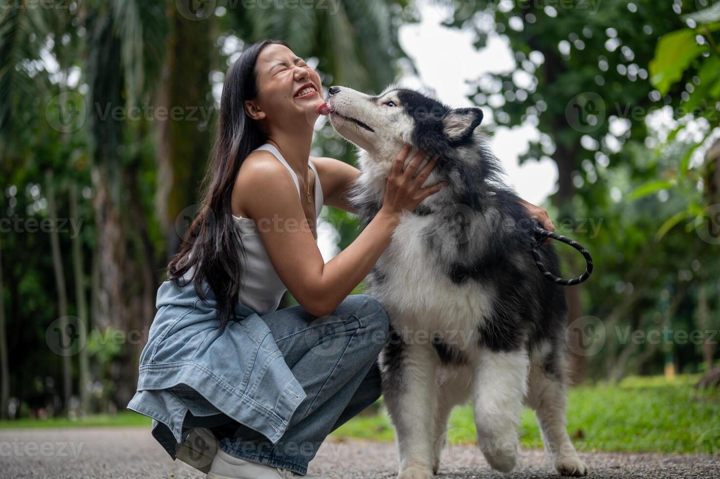 A woman is playing with her dog while taking it for a walk in a park. The dog licks her face. photo