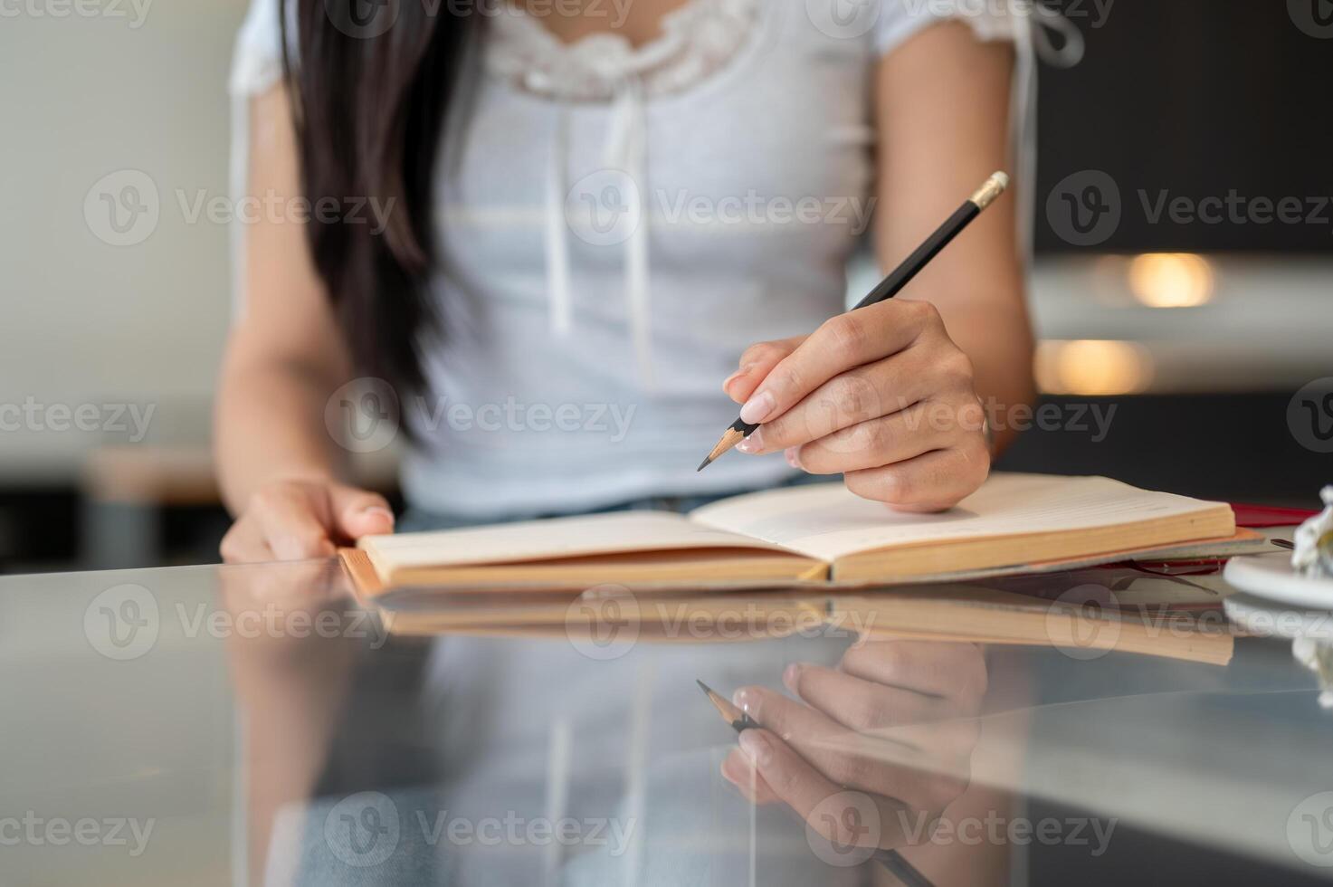 A close-up of a woman holding a pencil and writing in a book at a table indoors. photo