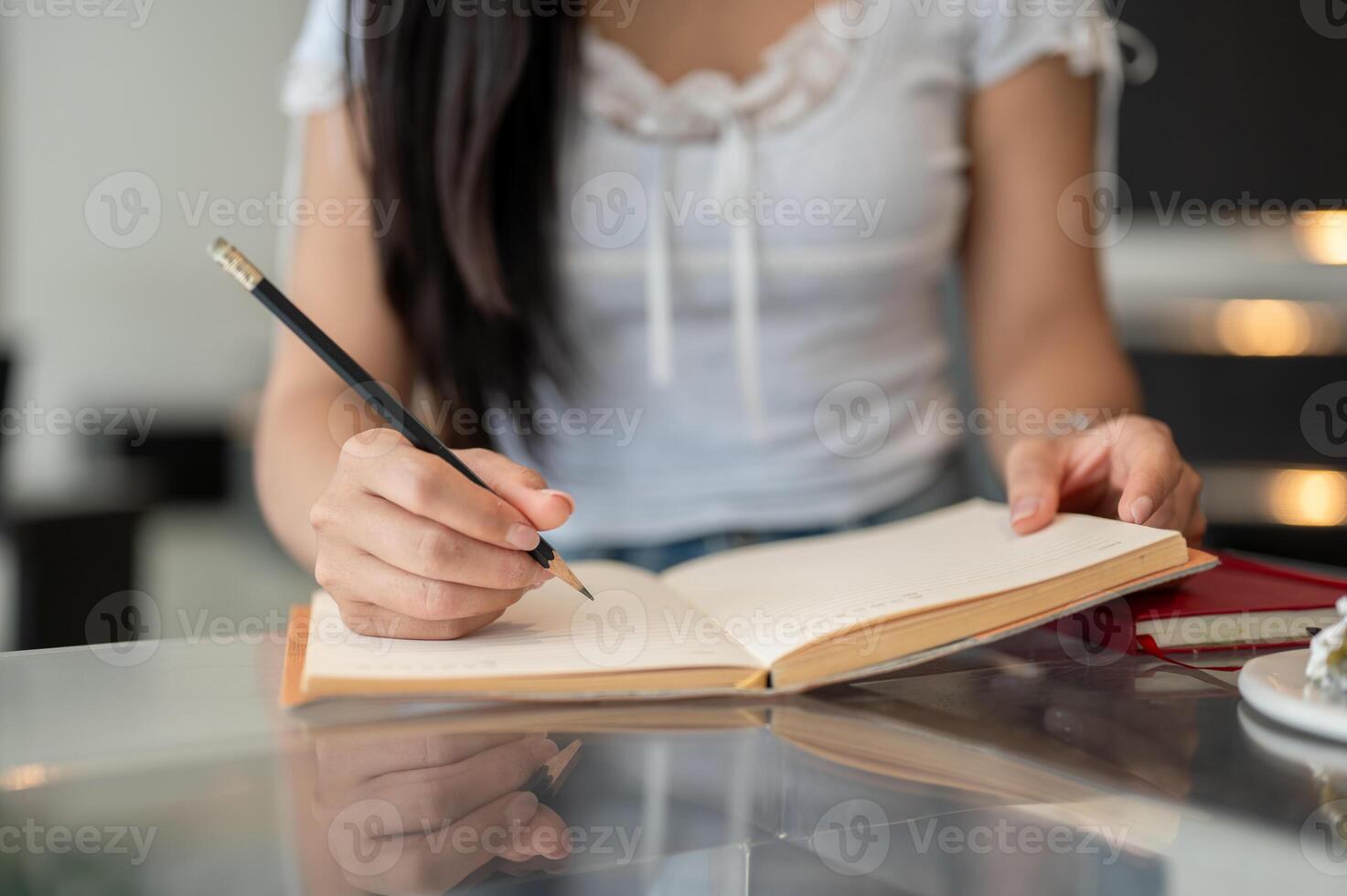 A close-up of a woman holding a pencil and writing in a book at a table indoors. photo