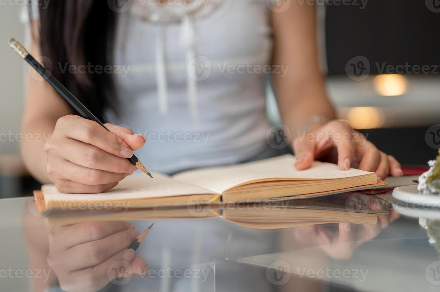 A close-up of a woman holding a pencil and writing in a book at a table indoors. photo