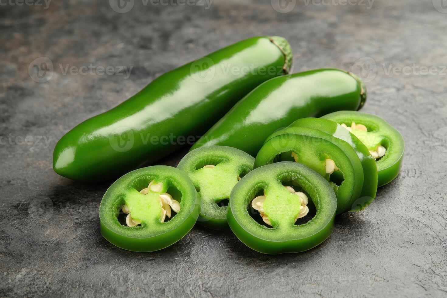 Fresh green jalapenos displayed on a dark stone surface, showcasing whole and sliced peppers for culinary use and preparation photo
