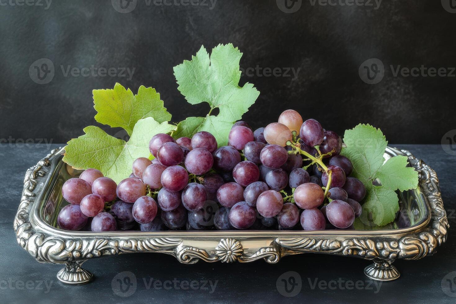 Freshly harvested purple grapes presented on a silver platter with green leaves in a rustic setting photo