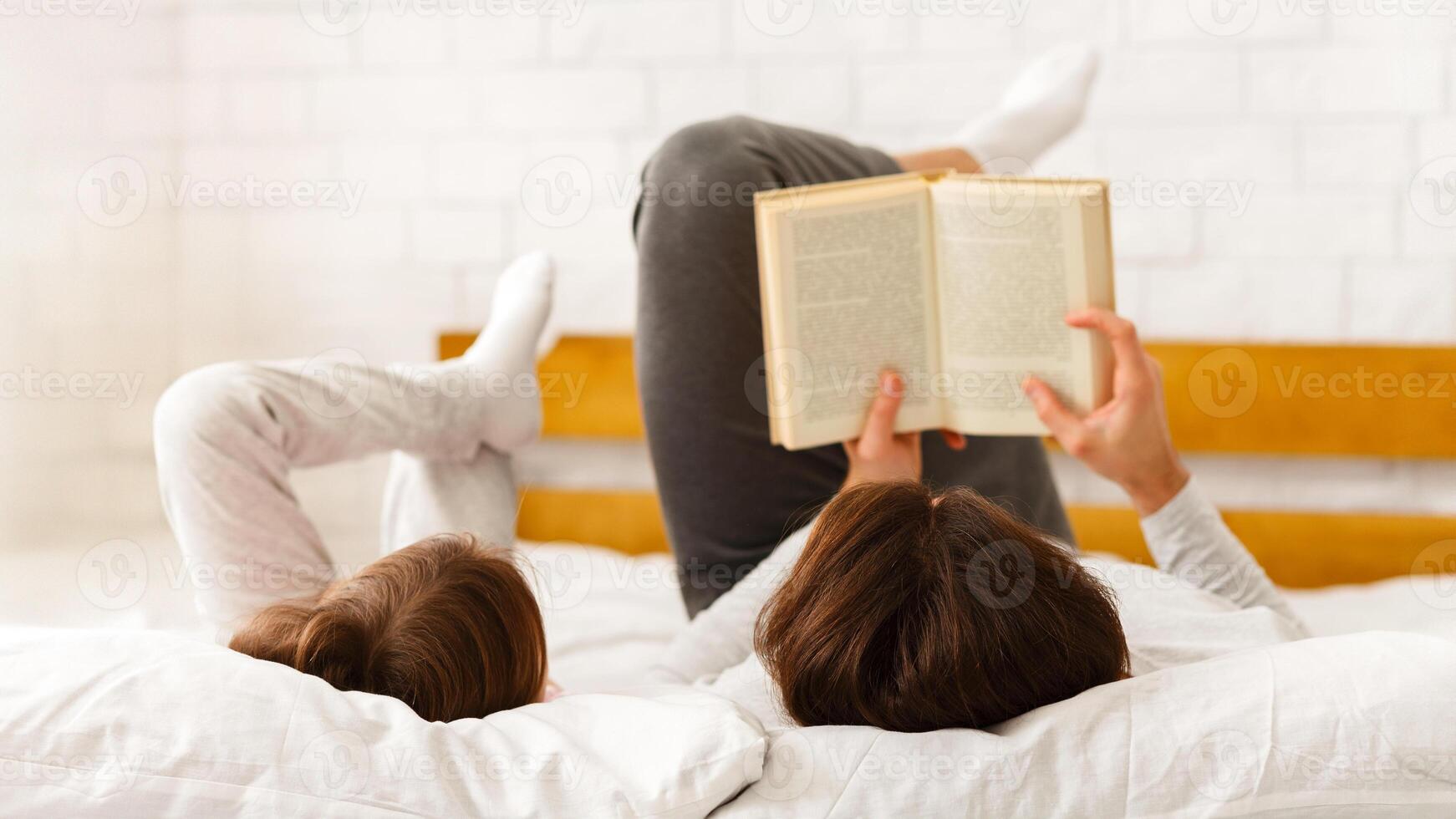 Father and little girl lying on bed, reading book on weekend photo