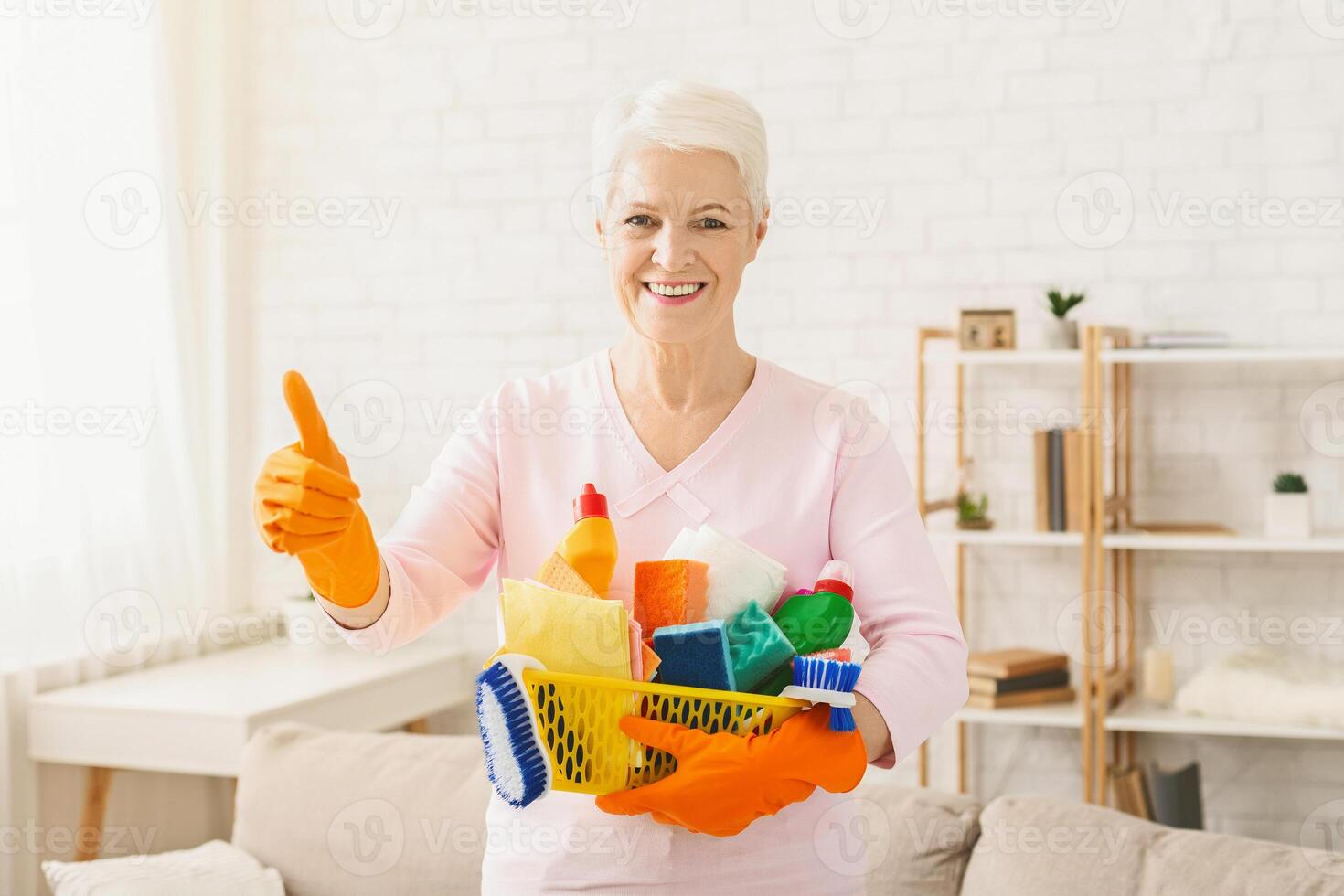 Cheerful senior woman with detergents variety showing thumb up, copy space photo