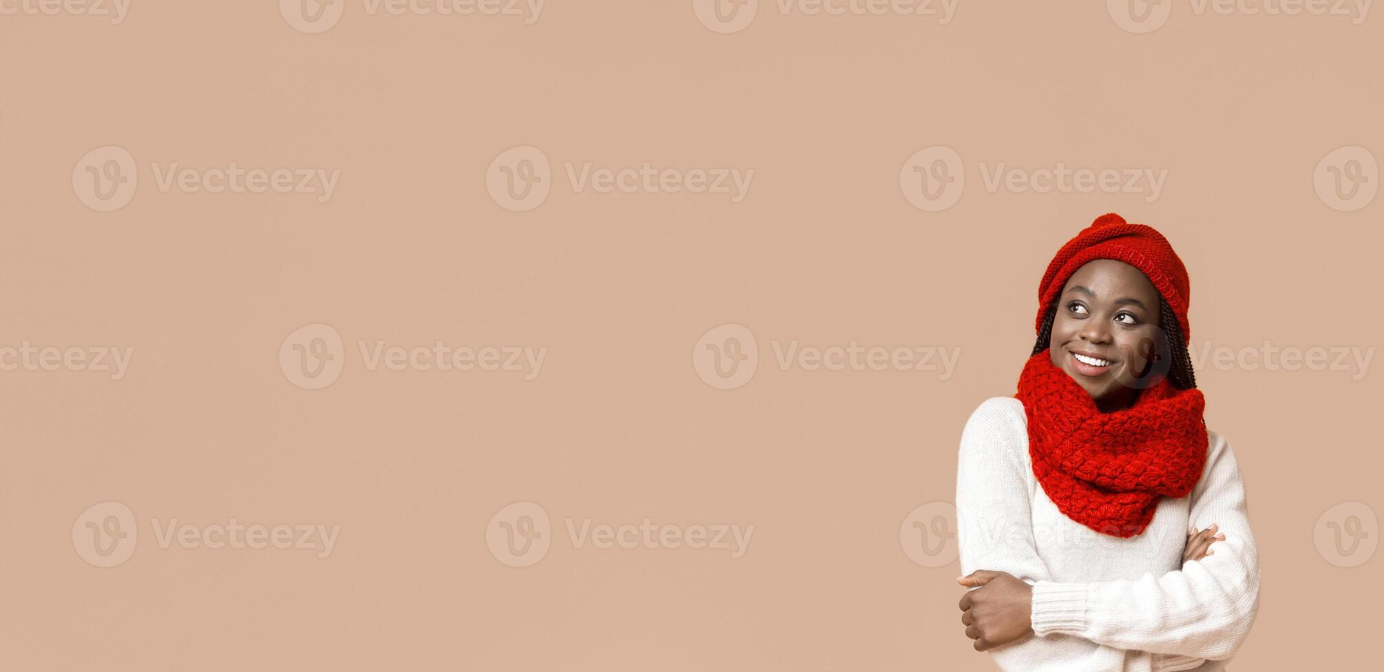 Confident smiling african woman in knitted red set looking at empty space over beige background photo