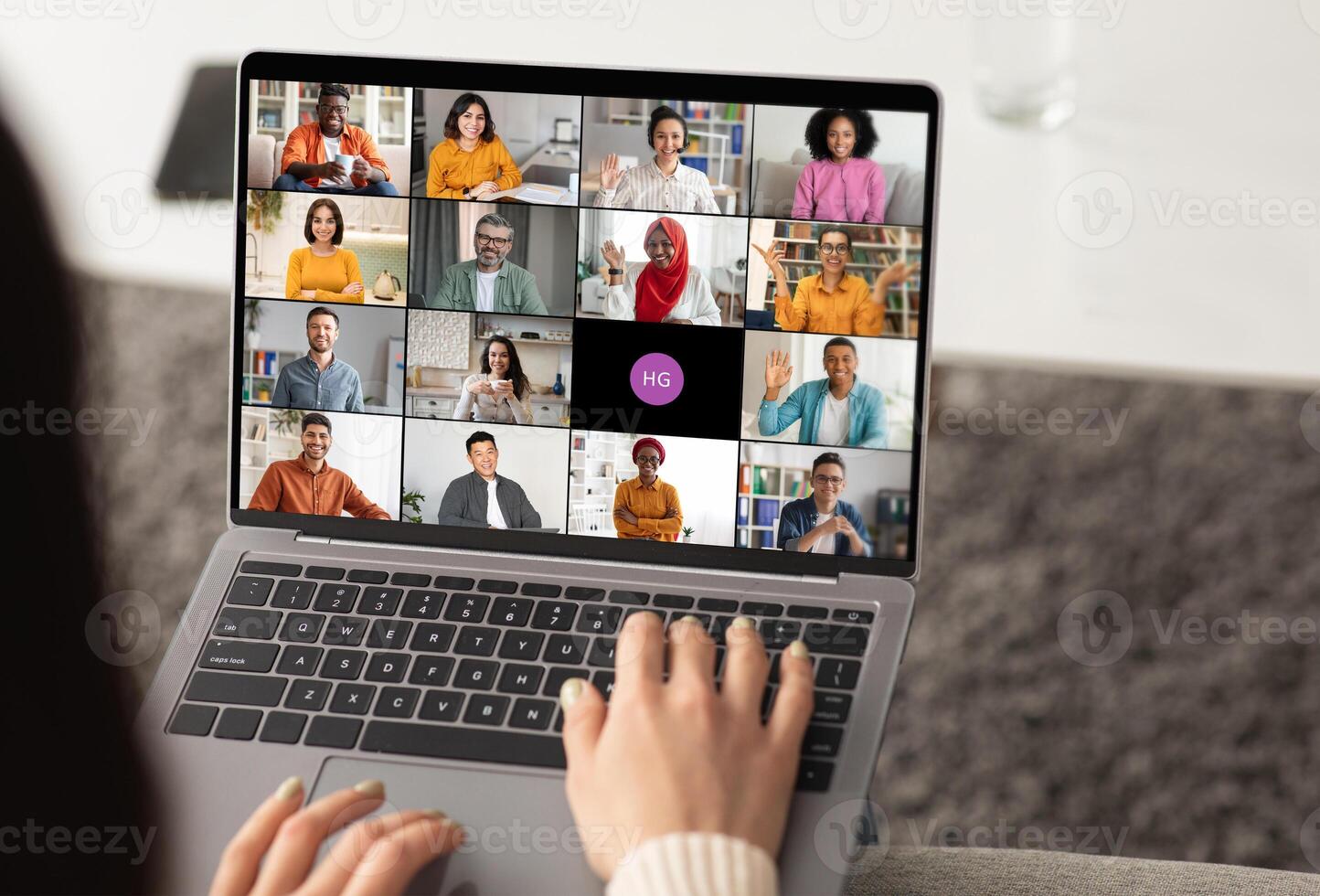 Woman using a laptop to participate in an online chat meeting. The screen displays several participants in a grid format, showcasing a diverse group of people. photo