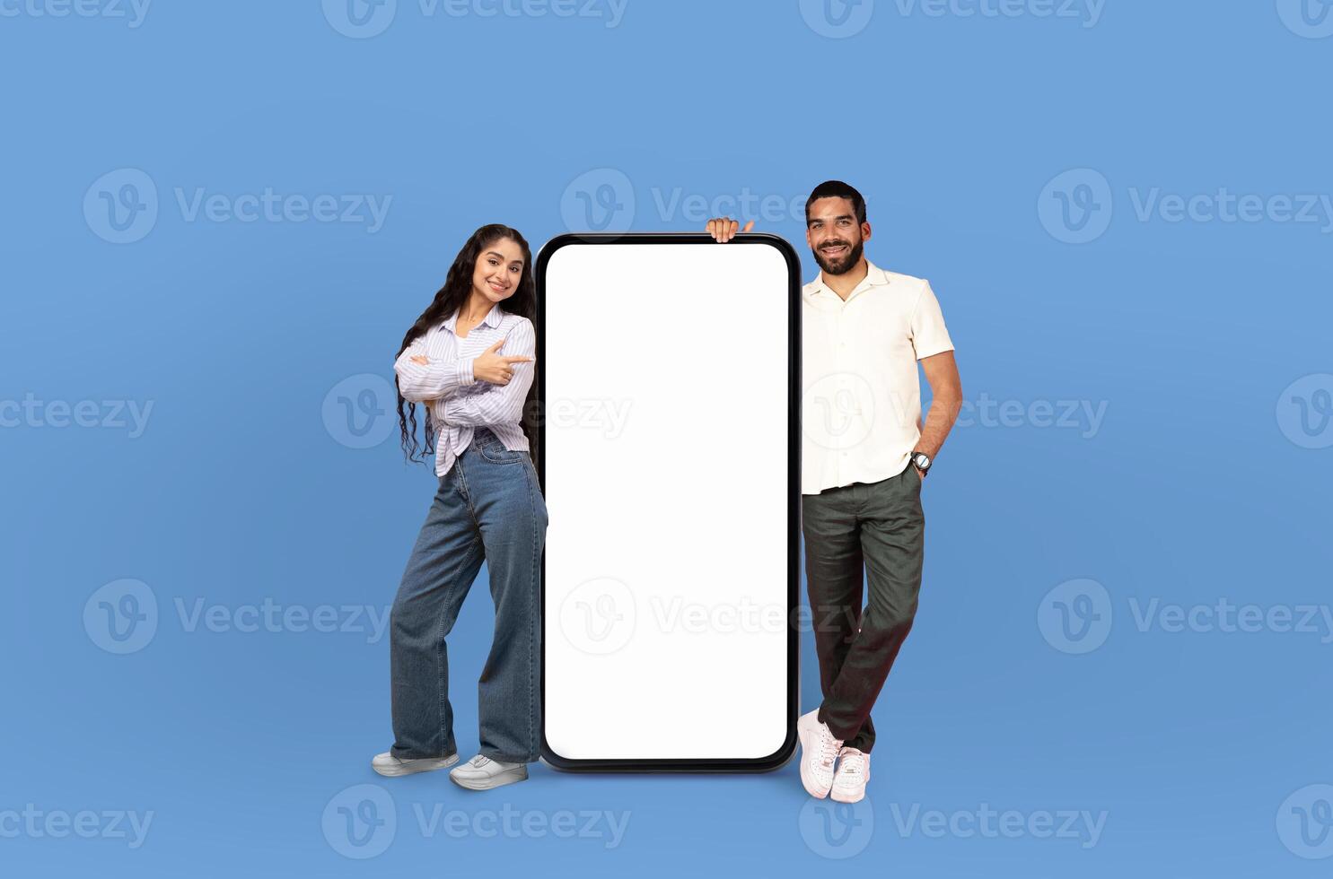 Together, the multiethnic cheerful couple showcase a large, blank smartphone screen, demonstrating a perfect template for digital innovation. photo