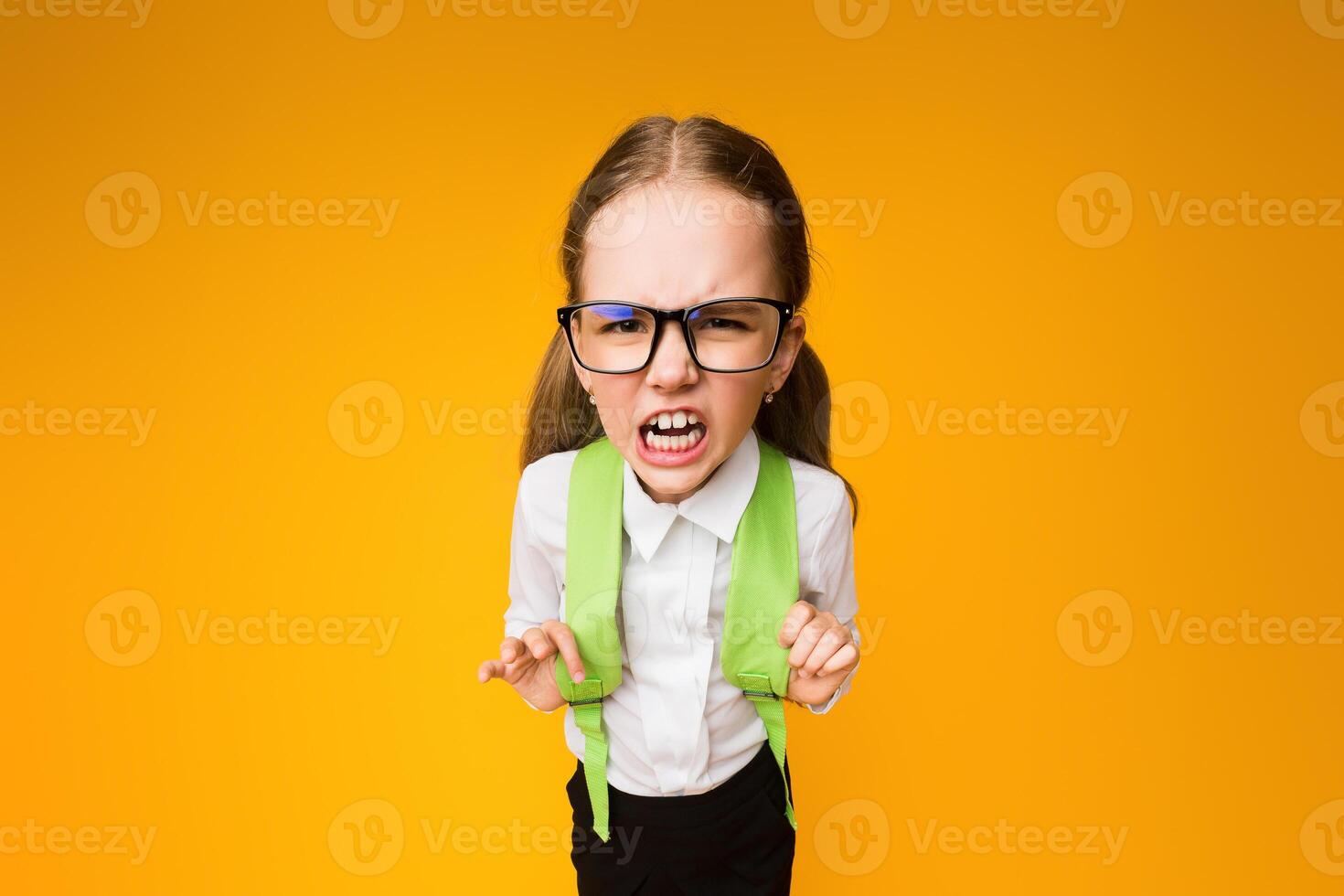 School Hate. Angry Schoolgirl In Eyeglasses Roaring And Frowning At Camera On Yellow Background. High-Angle Studio Shot photo