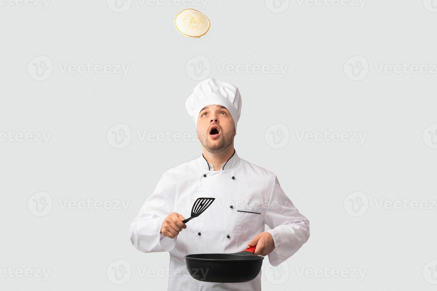 Cooking Food. Surprised Chef Man Holding Pan And Spatula Looking Up Standing Over White Background. Studio Shot photo