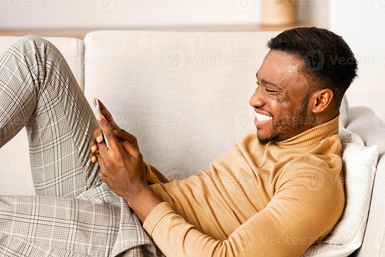Mobile App. Relaxed Black Guy Using Smartphone Playing Games Lying On Sofa At Home. photo