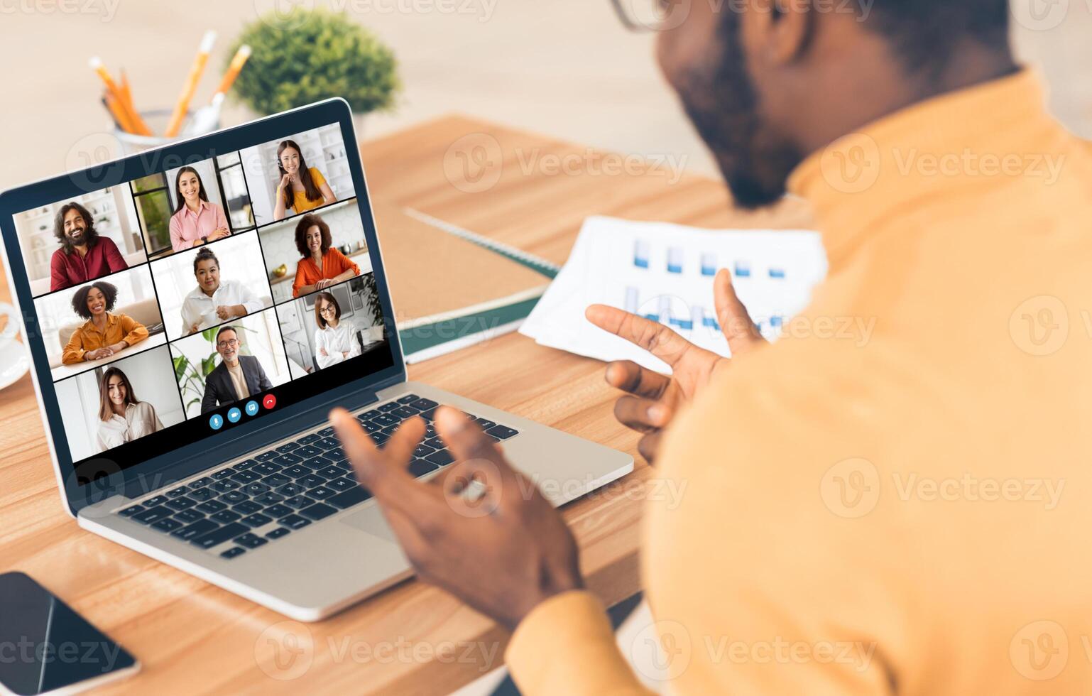 Black man sitting at a desk in front of a laptop, participating in a conference with his colleagues. He is gesturing with his hand and actively engaged in the conversation. photo