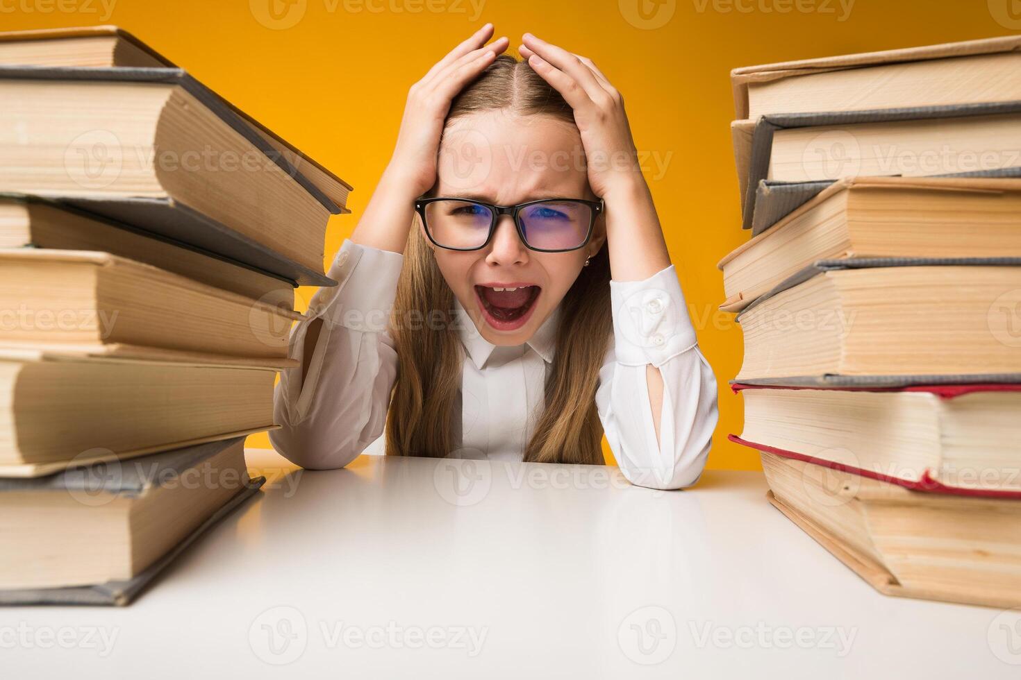 Back To School Stress. Little Girl Shouting Clutching Head Sitting Between Two Book Stacks On Yellow Studio Background. photo