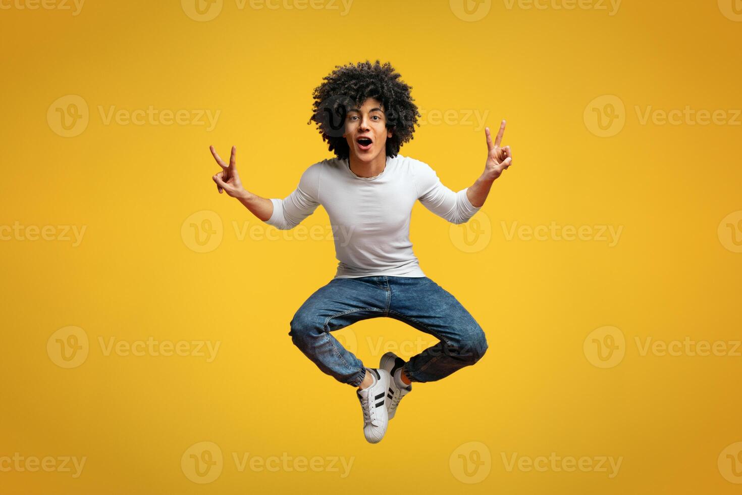 Enjoy your life. Happy joyful african-american man jumping up in air, demonstrating v-signs, orange studio background photo