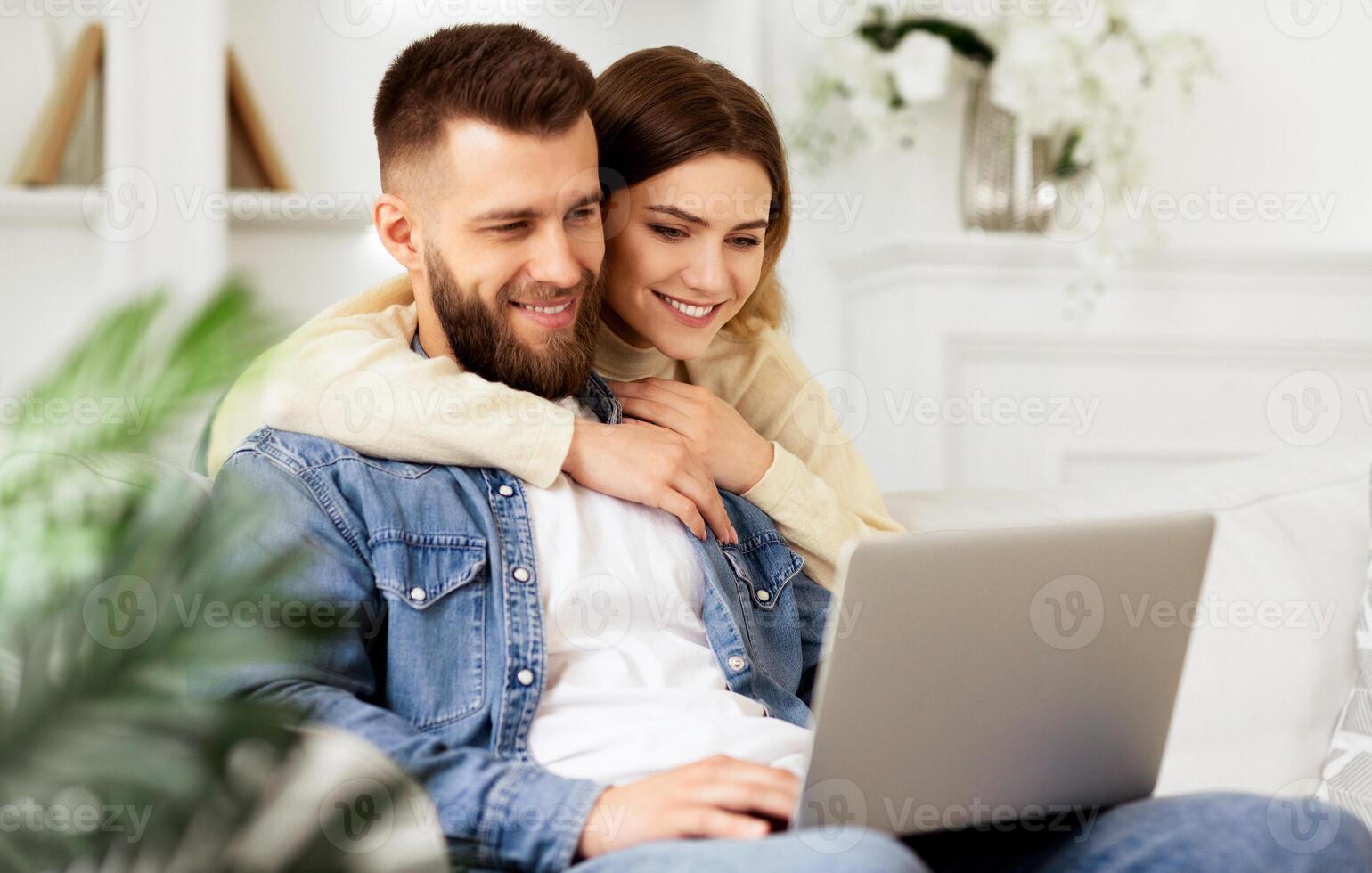 Loving Couple Having Video-Call On Laptop, Woman Hugging Husband, Relaxing At Home photo