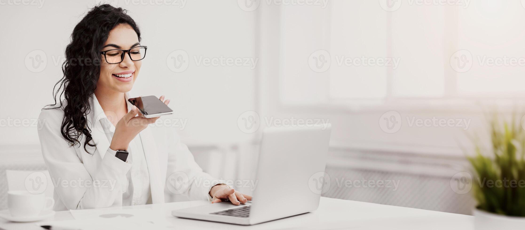 Voice Search. Mexican businesswoman using smart phone voice recognition to send message at workplace. Empty space photo