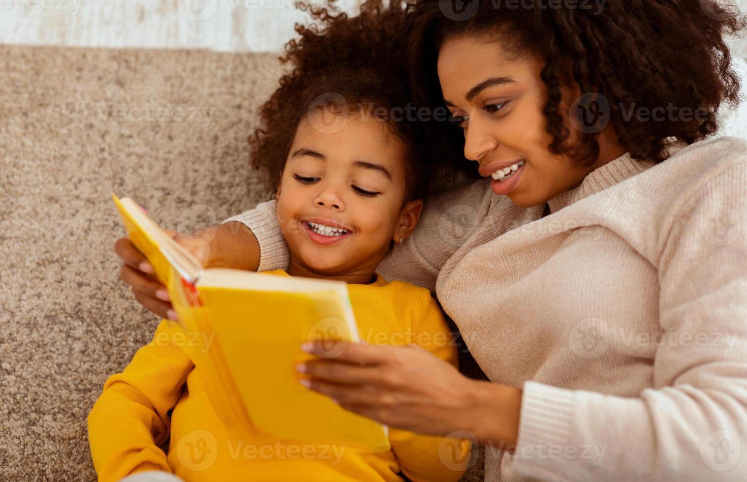 Cute Black Mother And Little Daughter Reading Book Together Sitting On Couch At Home. Bedtime Story Concept photo
