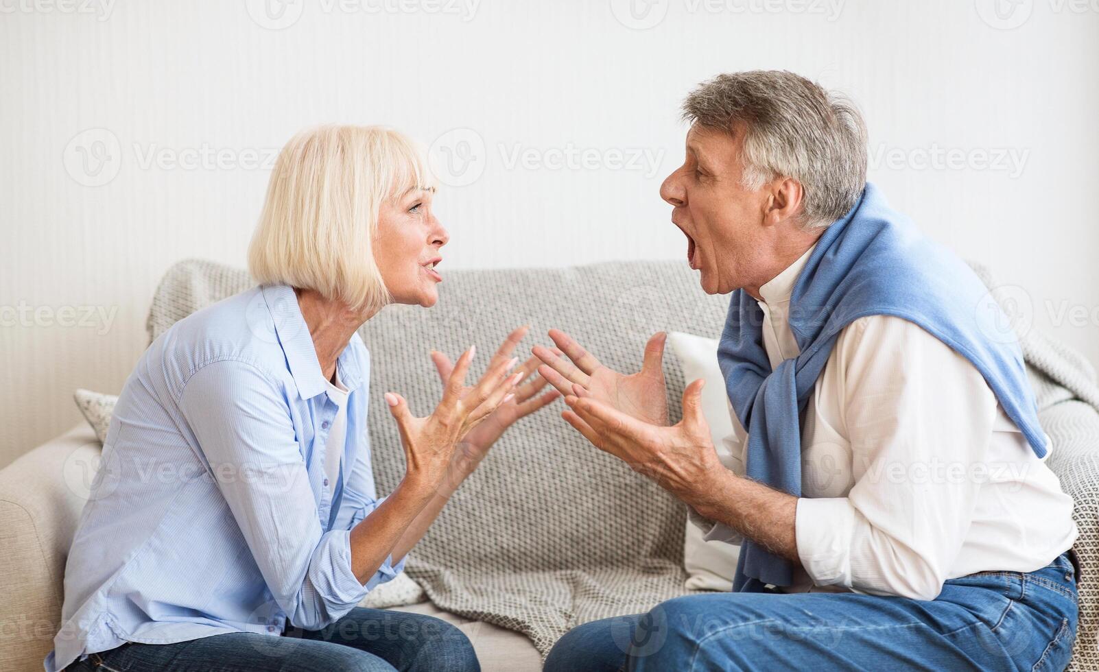 Senior couple quarrelling with each other and shouting, sitting on sofa at home photo