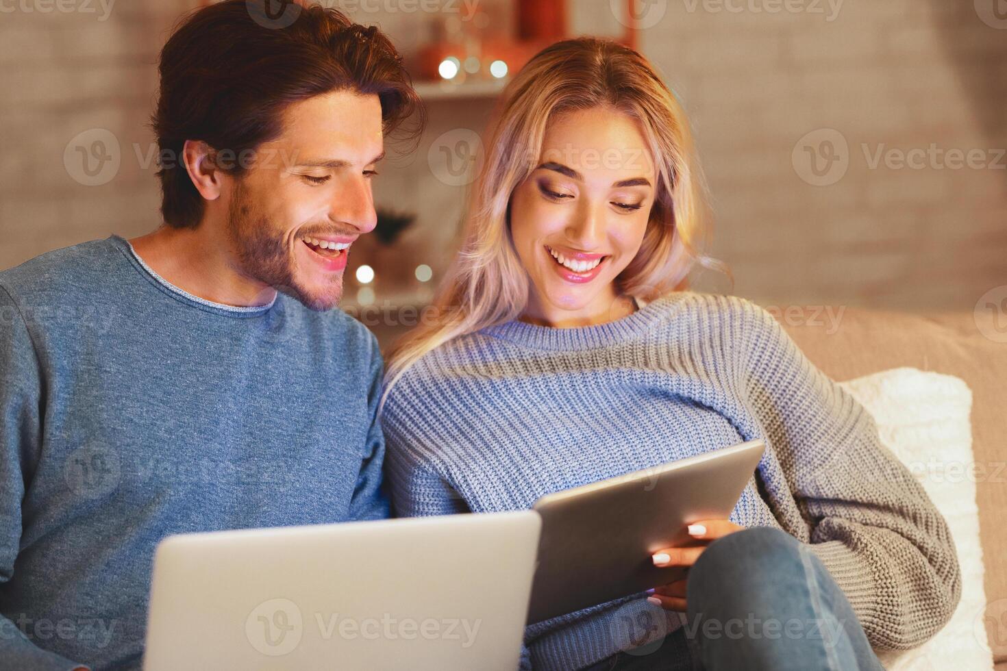 Modern Relationship. Relaxed Couple Using Tablet And Laptop Computers Sitting On Couch Indoor. Selective Focus photo