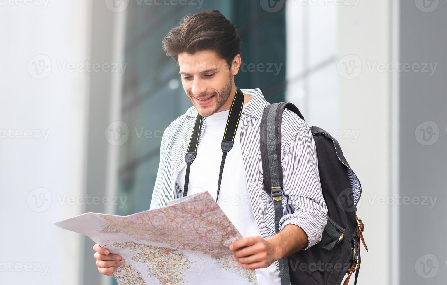 Happy Tourist. Smiling Young Man Standing Near Airport With City Map In Hands, Checking His Route, Empty Space photo