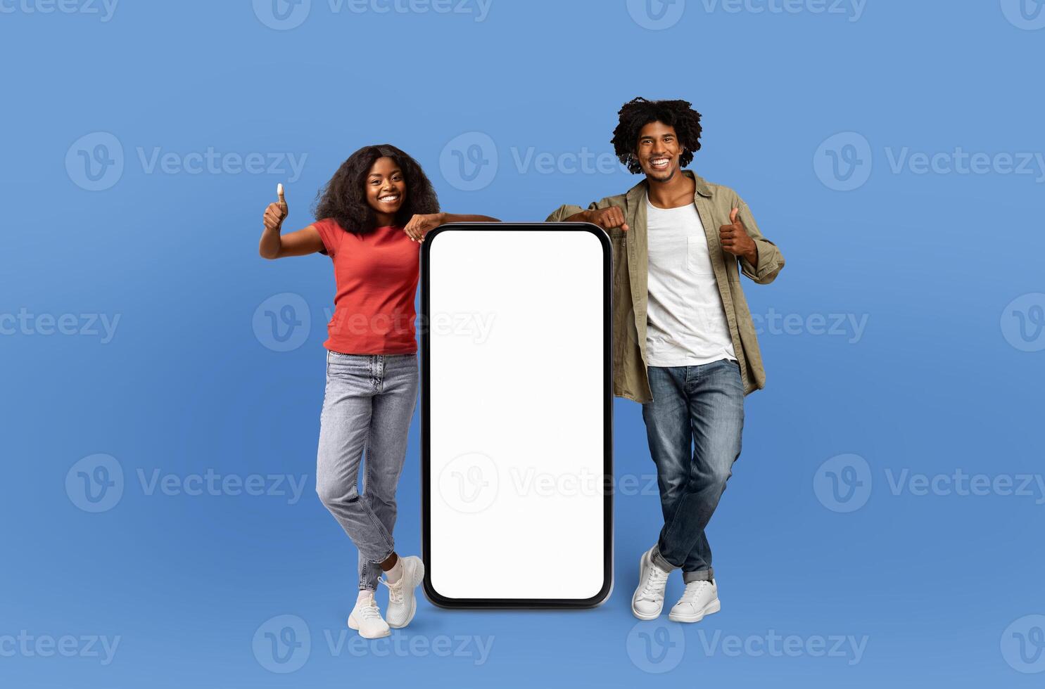 With joyful faces, the young African American man and woman pose beside a blank-screened, life-sized smartphone, emphasizing the endless possibilities for customization. photo