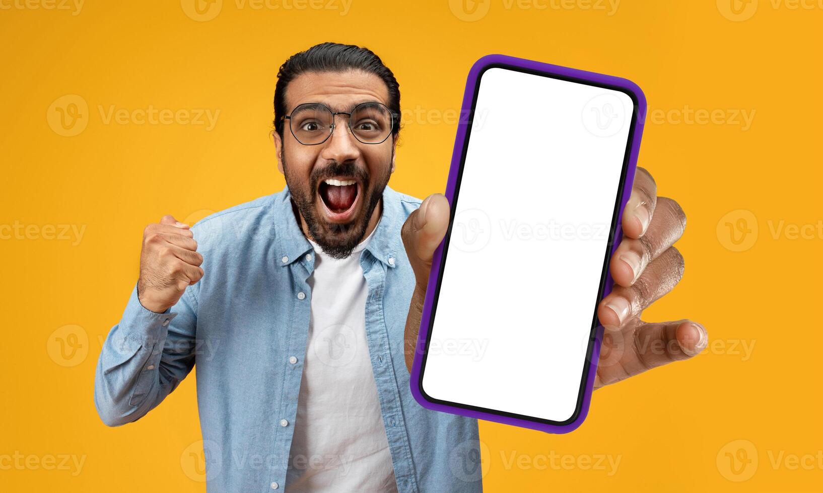 Indian man is holding up a cell phone in his hand, and his face displays a surprised expression. It seems that he has received unexpected news or seen something shocking on the screen. photo
