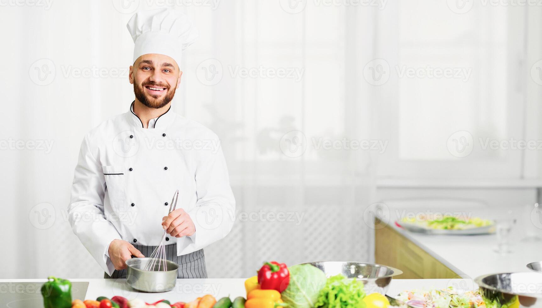 Chef Man Using Wire Whisk Mixing Ingredients In Saucepan Smiling At Camera Cooking Food In Restaurant Kitchen Indoor. Selective Focus photo