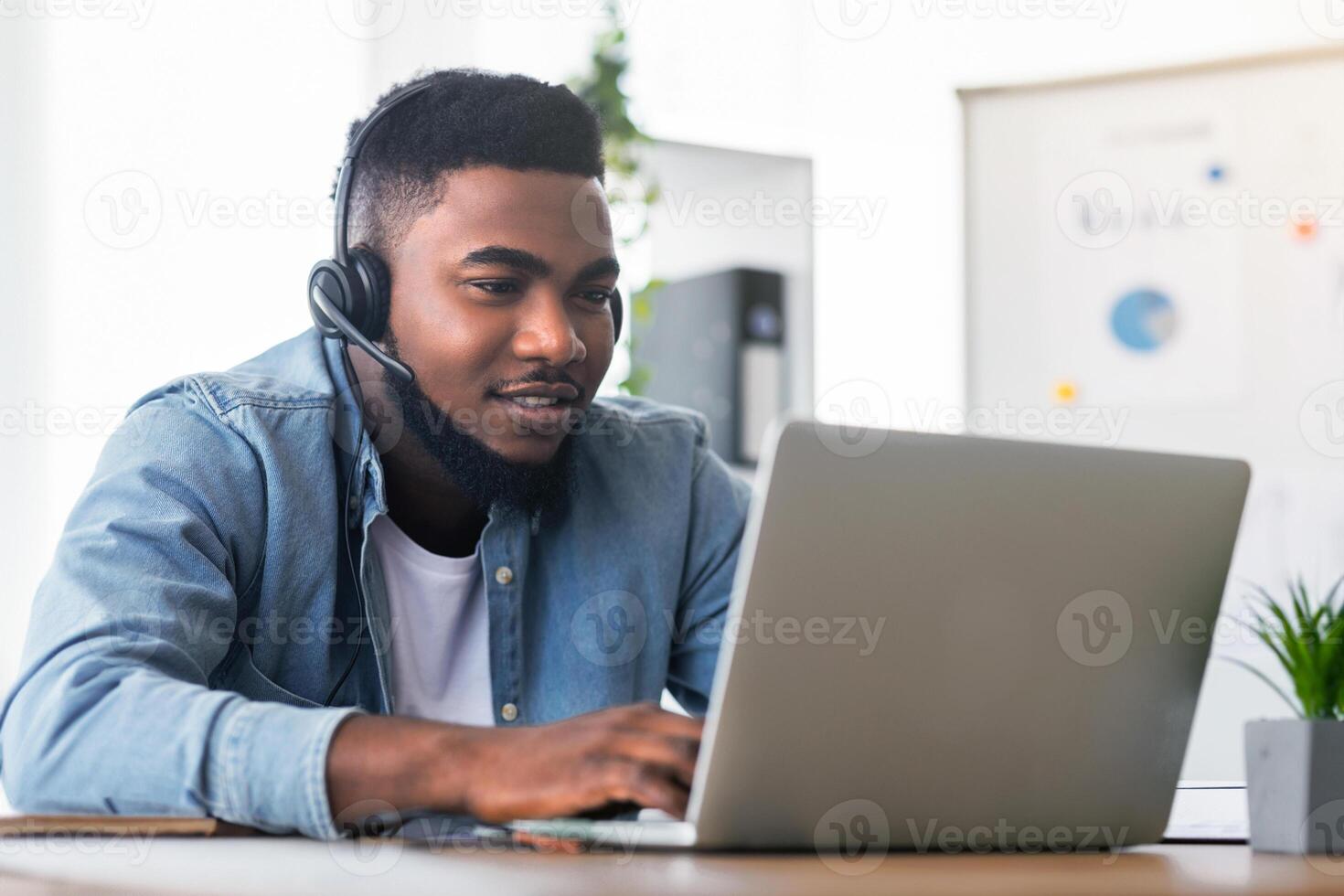Call center operator at work. Handsome black manager wearing headset and typing at laptop, working in modern office, free space photo