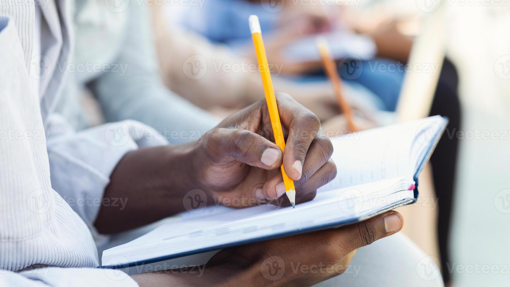 Cropped of black student guy taking notes, studying with friends, using notepad and pencil photo