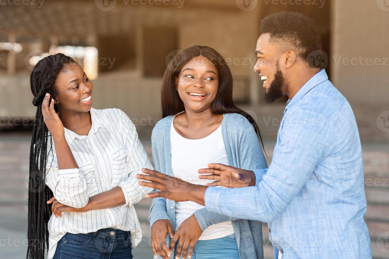 Three happy afro friends chatting and laughing outdoors in the street, handsome guy telling joke to girls, explaining something funny photo