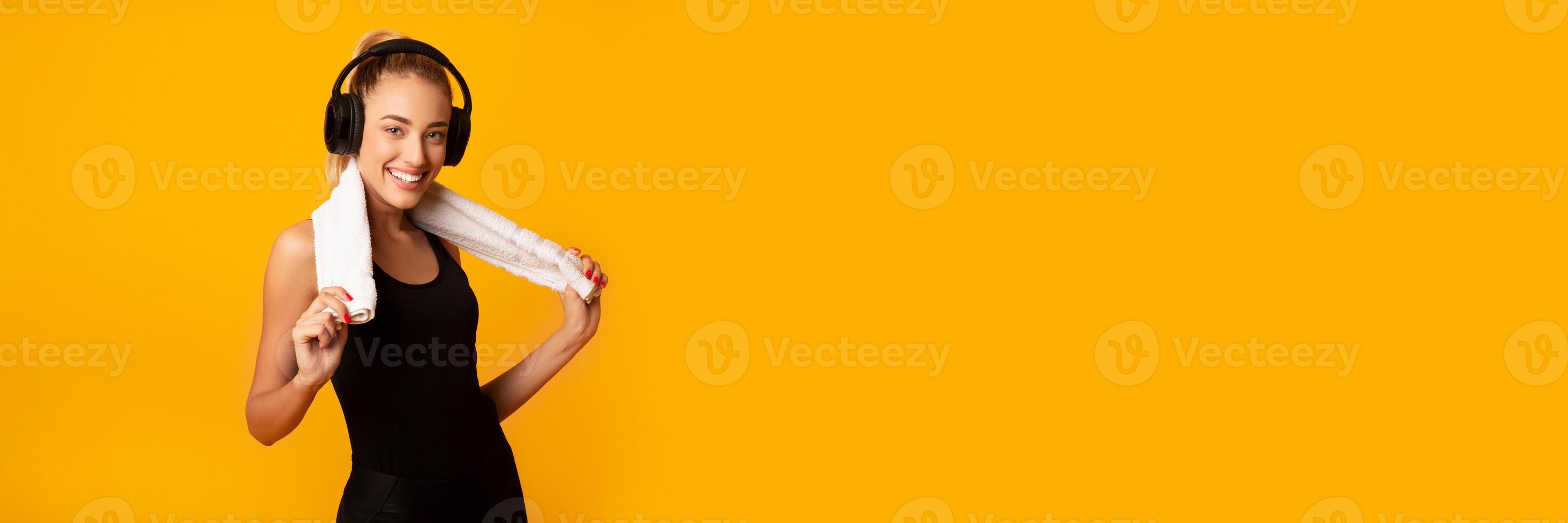 Smiling Fit Lady In Wireless Headphones Listening To Music After Fitness Workout Standing On Yellow Studio Background. Copy Space, Web-banner photo