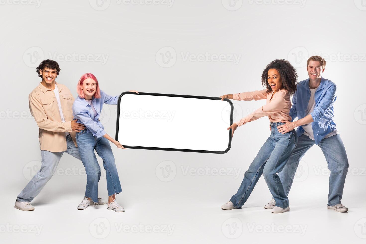 Four young adults, two women and two men, are holding a large smartphone with blank screen in front of a white background. photo